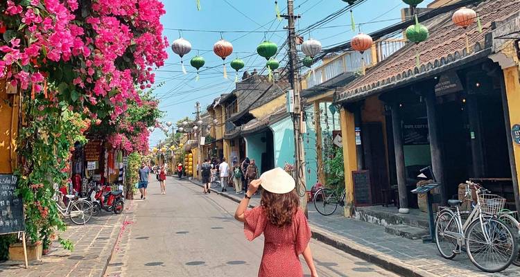 Vrouw met een hoed die door een kleurrijke straat met lantaarns loopt.