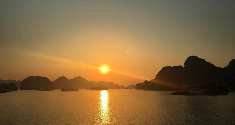 Coucher de soleil paisible sur une baie avec des bateaux et des formations karstiques.