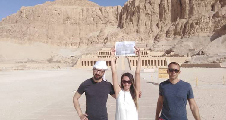 Drie mensen die een bord vasthouden met oude gebouwen op de achtergrond.