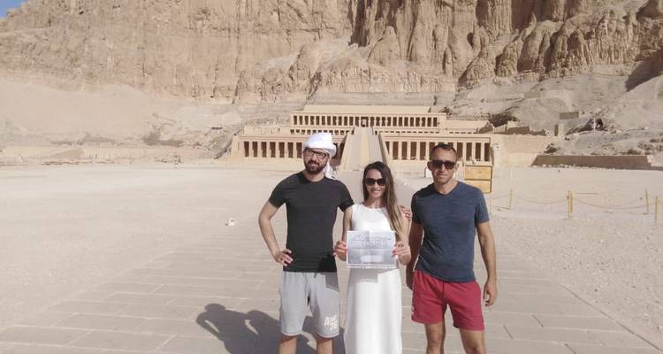 Drie mensen poseren voor oude bouwwerken.