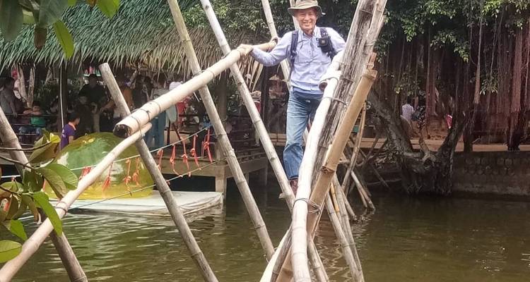 Man walking across a bamboo bridge over water.