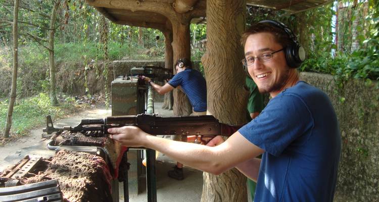 Tourist with headphones holding a gun at Cu Chi Tunnels shooting range.