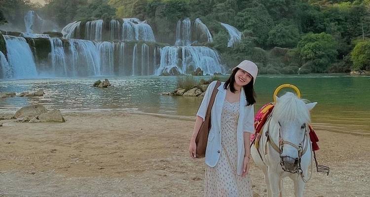 Femme posant avec un cheval blanc devant une grande cascade.