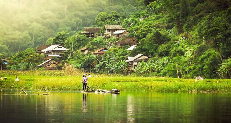 Une scène de village rural avec une personne sur un bateau dans une rivière.