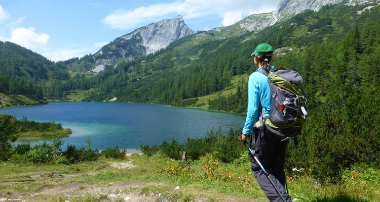 Randonneur debout près d'un lac avec un paysage de montagnes en arrière-plan.