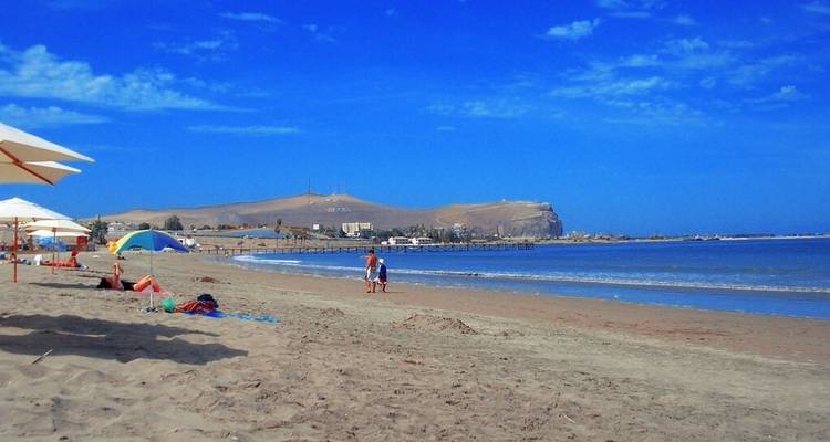 Ein sandiger Strand mit Menschen, die sich entspannen, und einer entfernten Landspitze.