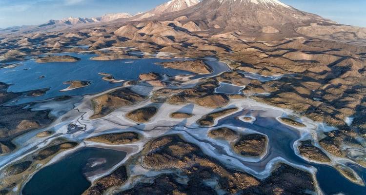 Luftaufnahme einer weiten, zerklüfteten Landschaft mit Seen und Bergen.