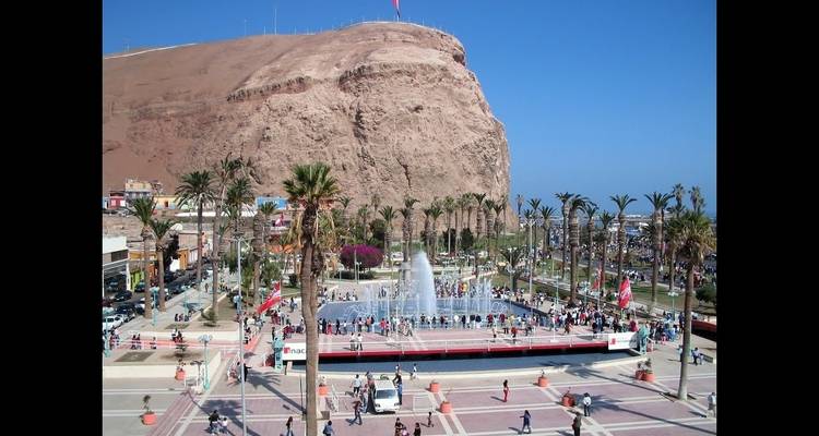 Ein belebter Platz mit einem Brunnen und einer großen Felsformation.
