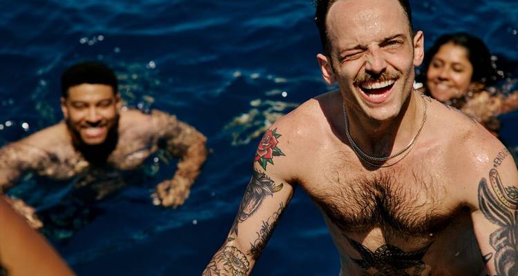 Laughing friends climb aboard a boat after a swim, with deep blue sea behind them.