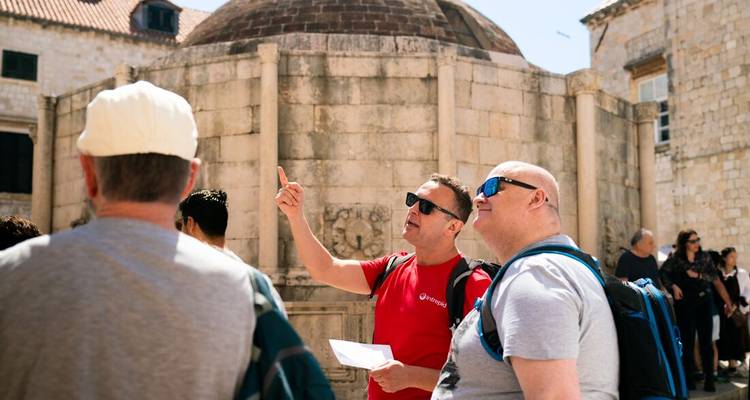 Guided tour group listens in front of Dubrovnik’s historic Onofrio Fountain and stone walls.