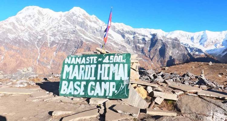 Schild zum Mardi Himal Basislager mit schneebedeckten Bergen im Hintergrund.