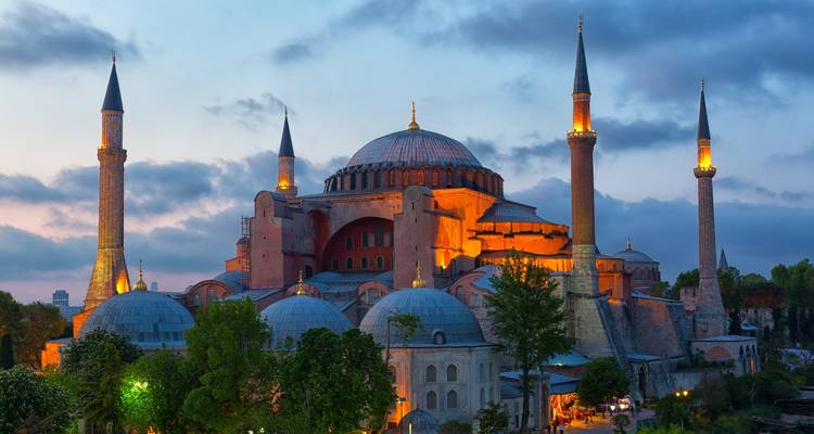 Hagia Sofía al atardecer con minaretes y cúpulas iluminados.