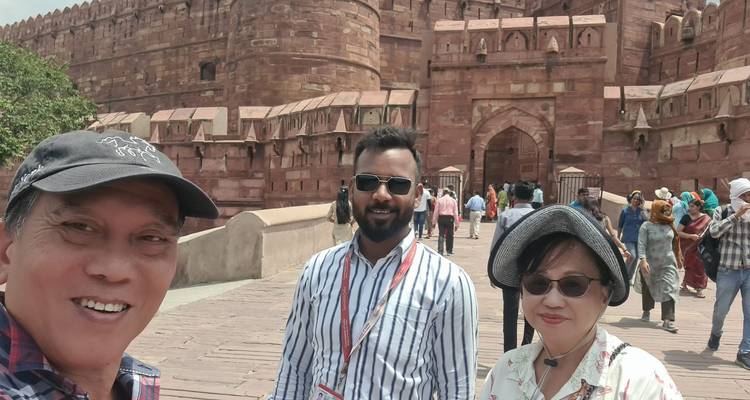 Groepsselfie voor een rood fort met veel mensen op de achtergrond.