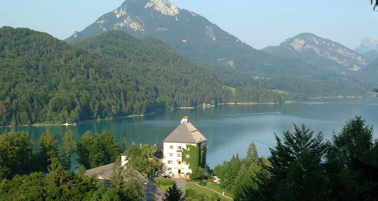 Vista panorámica de un lago y montañas con un edificio en primer plano.
