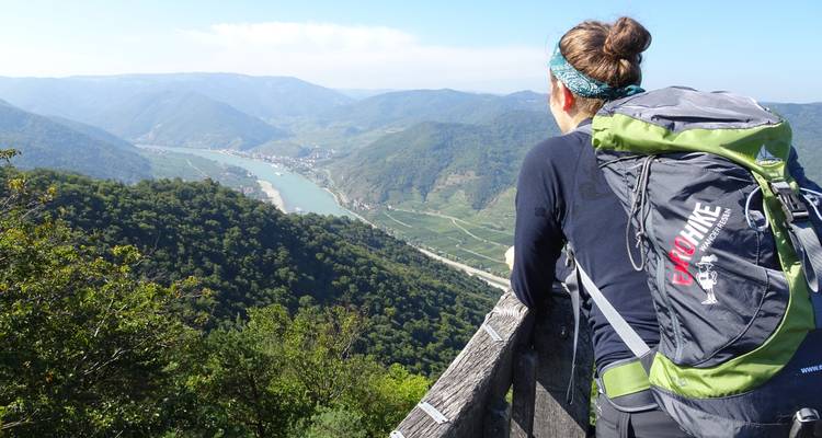 Persona con mochila contemplando un valle fluvial.