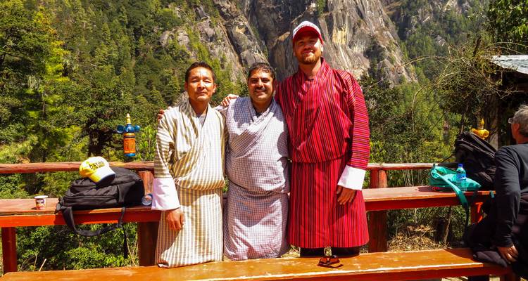 Tres hombres con vestimenta tradicional butanesa con un telón de fondo montañoso.