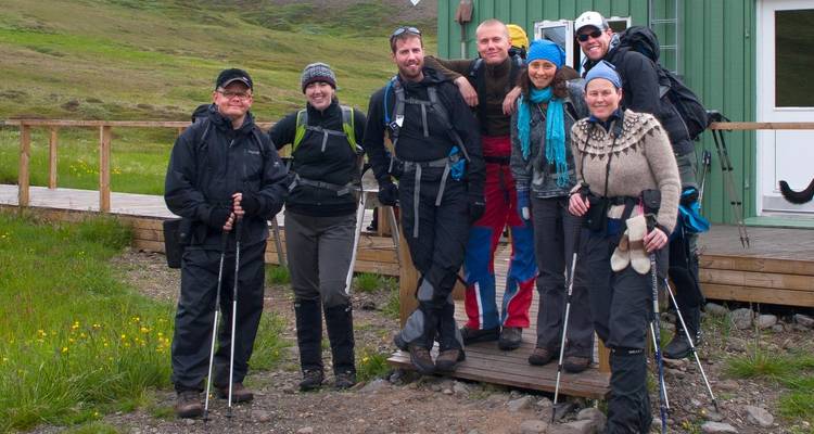 Group of hikers posing in front of a cabin in a grassy area.
