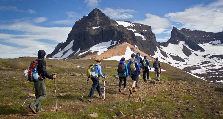 Hikers traversing a rocky landscape with a prominent snow-covered peak.