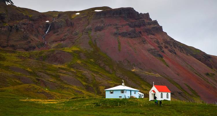 Small chapel and house near a colorful hillside.