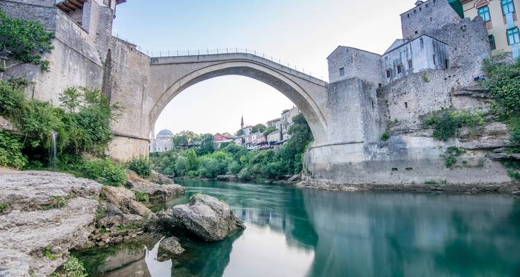Pont de pierre en arc au-dessus d'une eau calme, faisant partie d'une ville historique.