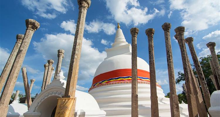 Weiße Stupa, umgeben von hohen Steinsäulen.