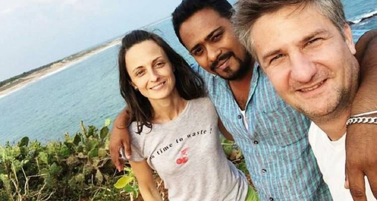 Drei Menschen posieren für ein Selfie mit einer malerischen Kulisse aus Ozean und Grünflächen.