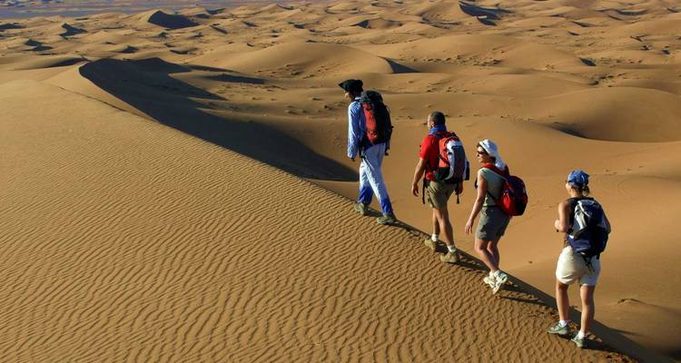 Wandelaars die langs zandduinen in een woestijn lopen.