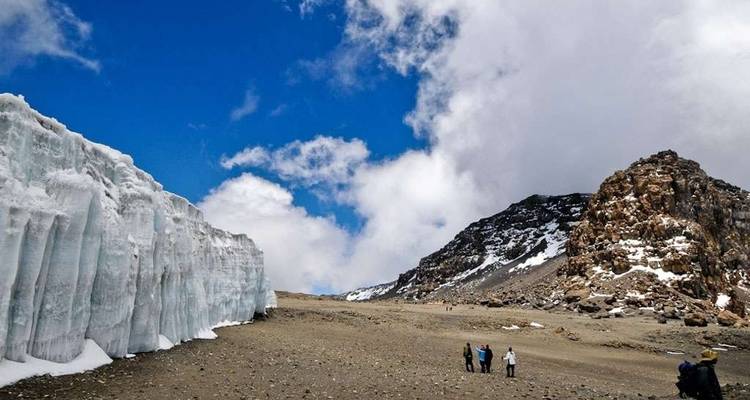 Hikers walking beside a glacier with a clear blue sky.