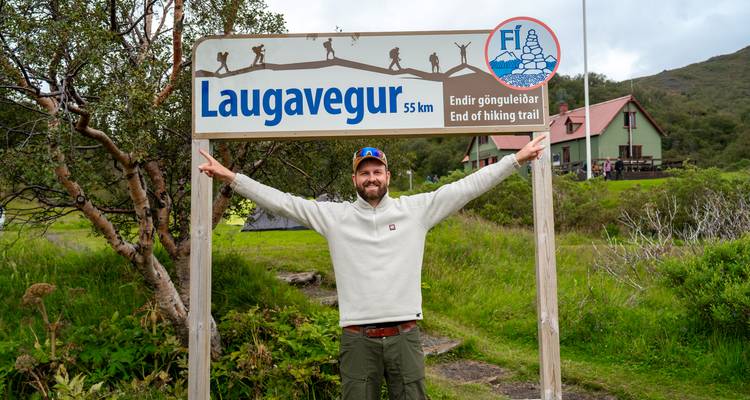 Le guide sourit sous le panneau de fin de sentier de Laugavegur en levant les deux bras