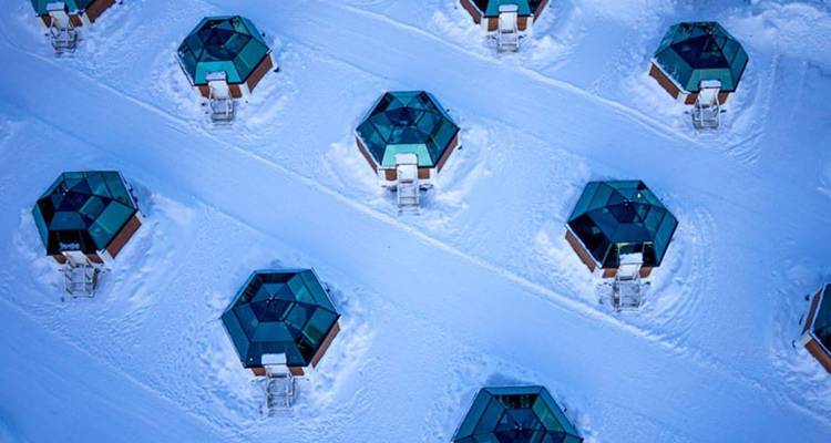 Vue aérienne de cabanes igloo aux toits de verre disposées dans un paysage enneigé en Laponie finlandaise.