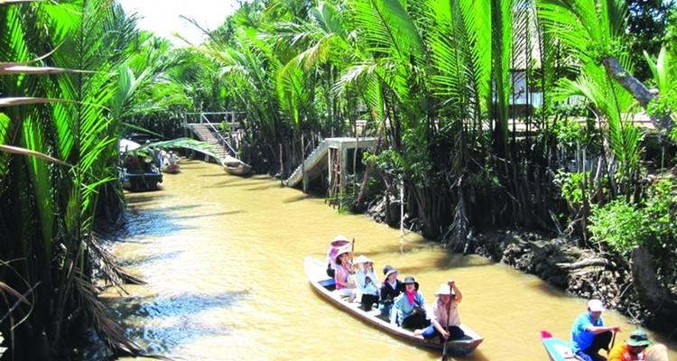 Personas remando botes por un río estrecho con vegetación.