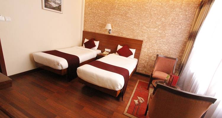 Hotelkamer met twee eenpersoonsbedden, houten vloer en een kleine zithoek.