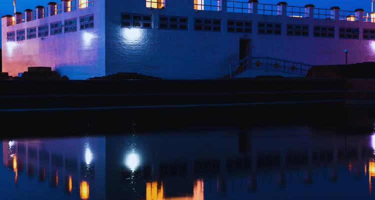 A building with blue lighting reflecting in a pond.