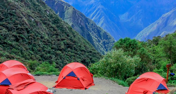 Carpas rojo brillante armadas en un campamento rodeado de empinadas montañas andinas verdes bajo un cielo despejado.