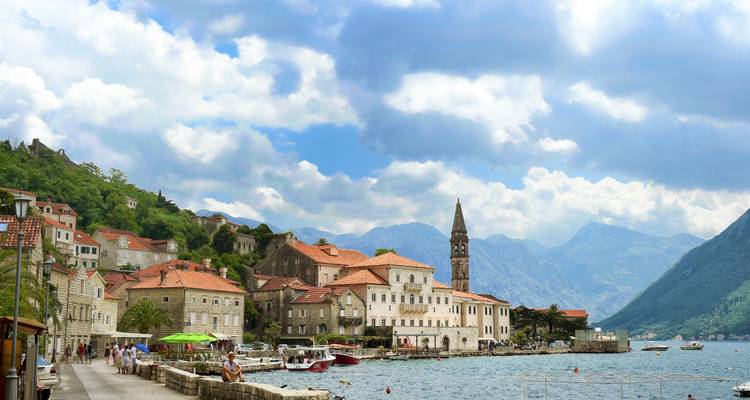 Coastal area with historic buildings, palm trees, and a view of mountains.