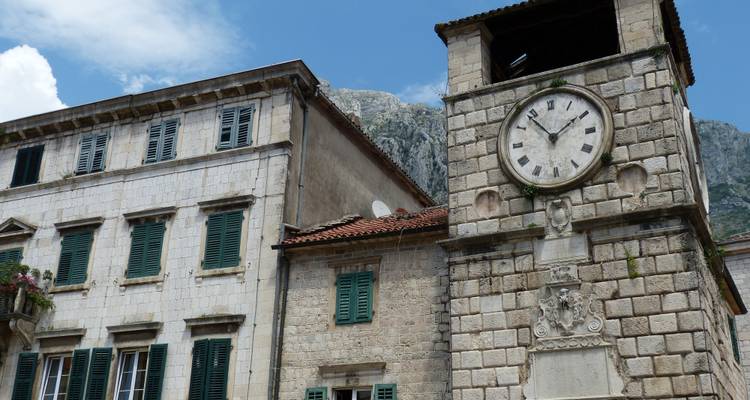Historic clock tower on an old stone building with green shutters.