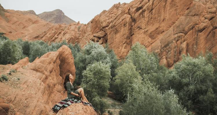 Eine Person, die auf einem Felsen in einer ruhigen Berglandschaft sitzt.