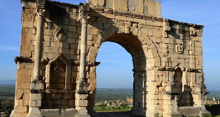 Antike römische Ruinen mit einem Torbogen und offener Landschaft.