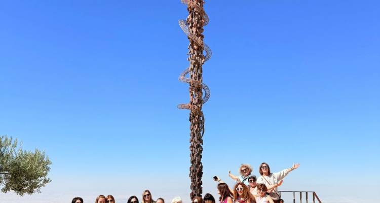 Groupe de touristes posant à côté d'une sculpture moderne en extérieur.