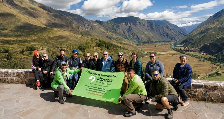 El grupo muestra el estandarte de Alpaca Expeditions con las montañas del Valle Sagrado de fondo.