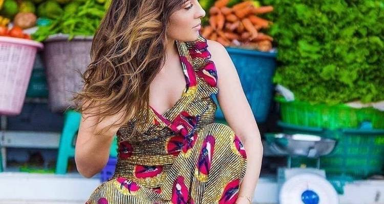 Femme qui pose dans une robe colorée devant un étal de légumes.