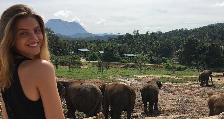 Une femme souriante avec des éléphants et des montagnes en arrière-plan.