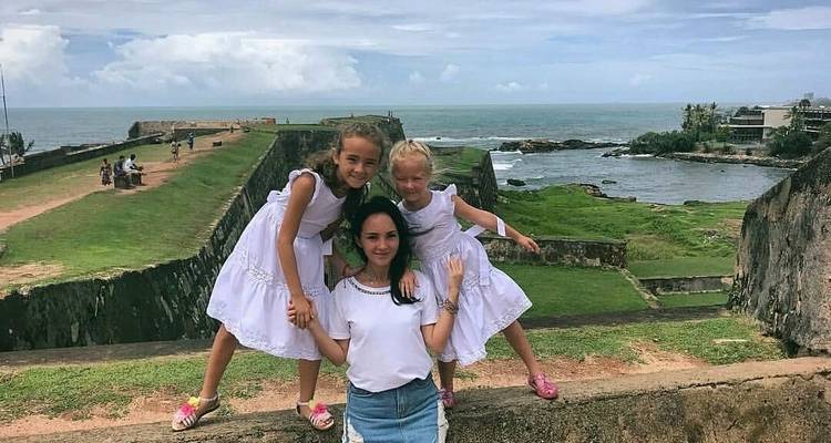 Une femme avec deux enfants posant sur un vieux fort surplombant la mer.