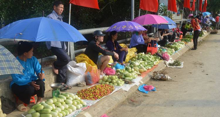 Straatmarktverkopers die onder parasols zitten en groenten en fruit verkopen.