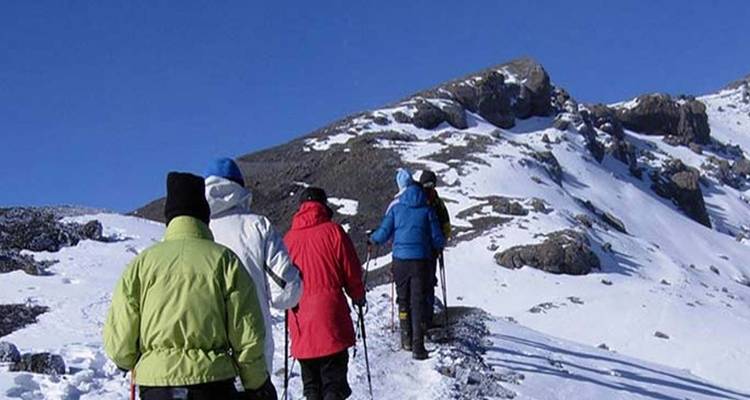 Randonneurs marchant le long d'une crête enneigée avec un sommet de montagne.