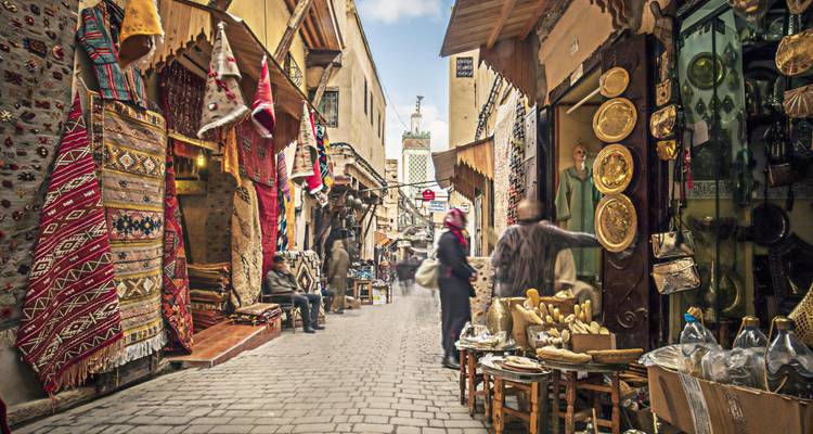 Calle de mercado bulliciosa con textiles vibrantes y diversos productos.