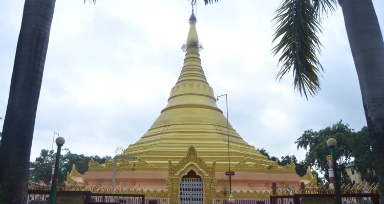 Goldene Stupa umgeben von Palmen und einem bewölkten Himmel.