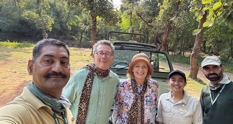 Groupe de safari souriant posant devant un jeep ouvert dans une clairière en forêt.