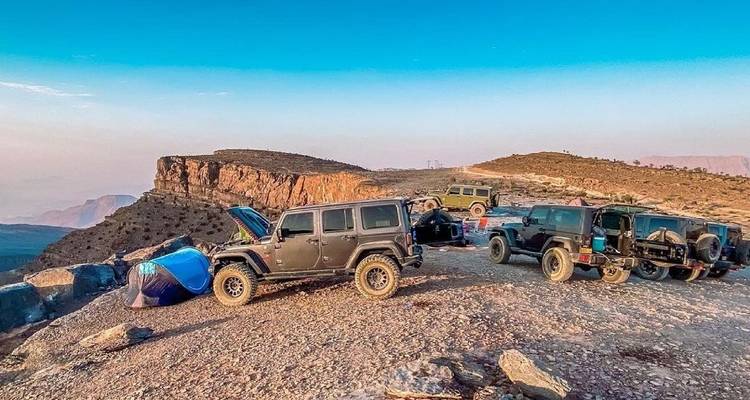 Grupo de vehículos todoterreno estacionados en un terreno rocoso con vista distante de montañas.