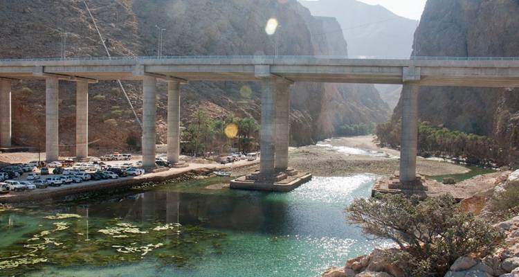 Puente sobre un río en un cañón con autos estacionados a un lado.